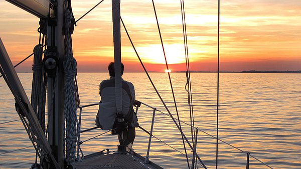 Person blickt vom Boot einer Yacht aus in Richtung Sonnenuntergang