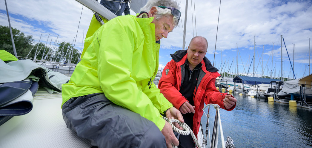Skipper erklärt zwei Männern auf einer Segelyacht einen Knoten